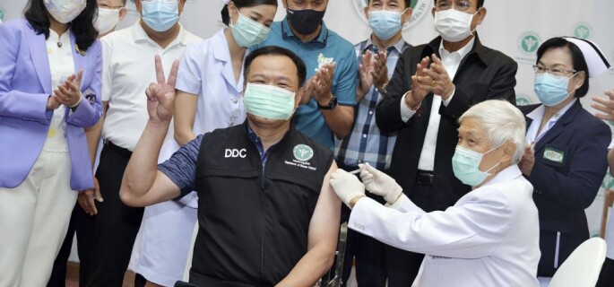 In this photo released by Government Spokesman Office, Thailand's Prime Minister Prayuth Chan-ocha, second right in the background, claps his hands after Thailand's Public Health Minister Anutin Charnvirakul received the first China's Sinovac vaccine at Bamrasnaradura Hospital in Bangkok, Thailand, Sunday, Feb. 28 , 2021. (Government Spokesman Office via AP)